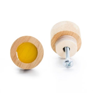 Könnte beinhalten: Zwei Holzknöpfe mit einem gelben Kreis in der Mitte. Ein Knopf ist mit einer Schraube befestigt.