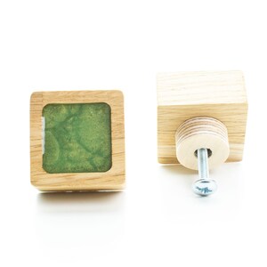 May include: Two wooden cabinet knobs with a square shape. One knob has a green resin insert. The other knob has a screw attached.