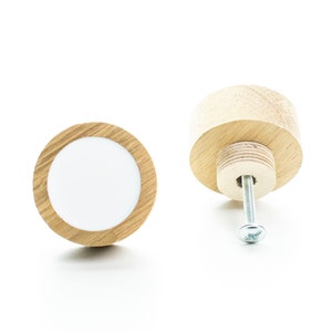May include: A round wooden knob with a white centre and a screw for attaching it to a surface. The knob is made of light wood and has a natural finish.
