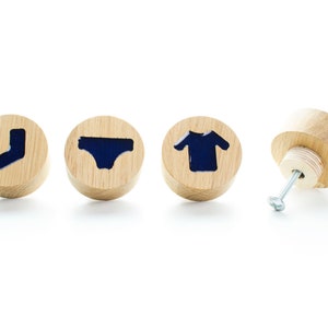 May include: Four wooden knobs with different clothing silhouettes in blue. The knobs are round and have a screw on the back.