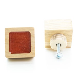 May include: Two wooden cabinet knobs with a square shape. One knob has a red square insert and the other has a silver screw.