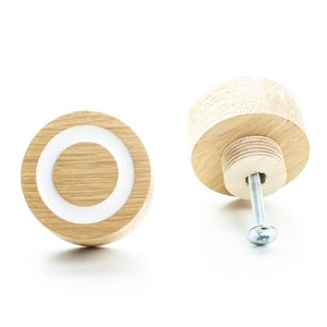 Può includere: Due pomelli per armadi in legno con un design a cerchio bianco. I pomelli sono rotondi e hanno una vite sul retro.