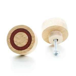 Può includere: Due pomelli per armadi in legno con un design a cerchio rosso. Un pomello è mostrato di lato con una vite fissata. L'altro pomello è mostrato dall'alto.