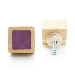 May include: Two square wooden cabinet knobs with a purple resin insert. One knob has a screw attached.