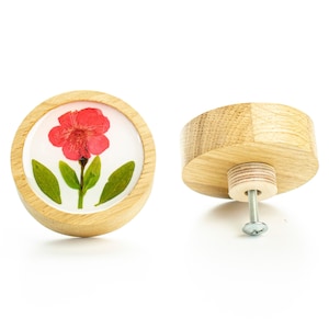 Op de afbeelding: Een ronde houten knop met een geperst bloemenmotief. De knop heeft een witte achtergrond met een roze bloem en groene bladeren. De achterkant van de knop toont de schroefbevestiging.