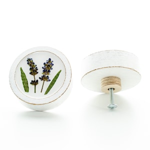 Könnte beinhalten: Weißer runder Knopf mit einem getrockneten Lavendelblüten-Design. Der Knopf hat eine Holzbasis und eine Schraube zum Befestigen an einer Oberfläche.