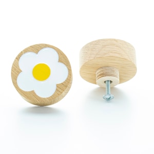 Könnte beinhalten: Zwei Holzknöpfe mit einem weißen Gänseblümchen-Design und einer gelben Mitte. Der Knopf links zeigt die Vorderseite des Knopfes, während der Knopf rechts die Rückseite des Knopfes mit einer Schraube zeigt.