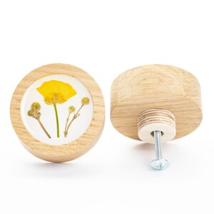 Peut inclure: Deux boutons ronds en bois, l'un avec une fleur jaune pressée sur le devant. Les boutons ont une vis au dos pour les fixer à un tiroir ou une armoire.