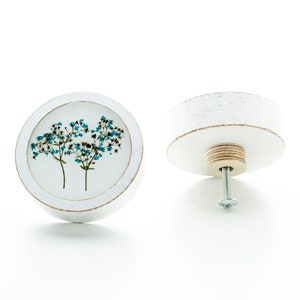 Peut inclure: Bouton rond en bois blanc avec un motif de fleurs bleues. Le bouton a une vis au dos pour le fixer à un tiroir ou une armoire.