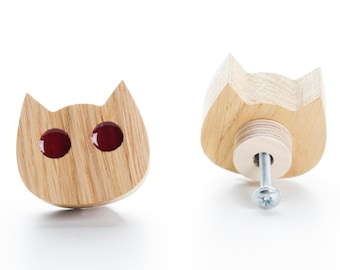 May include: A wooden cat-shaped drawer pull with red glass eyes. The pull is shown from the front and back.