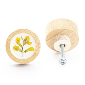 May include: A round wooden knob with a yellow flower pressed into the center. The knob has a silver screw for attaching it to a drawer or cabinet.