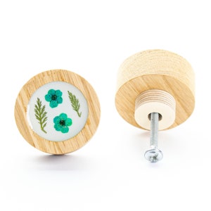 以下が含まれることがあります： 丸い薄い木製の土台と、ターコイズブルーの花と緑の葉がついた透明な樹脂のトップを持つ木製ノブ。ノブには銀色のネジが付いています。