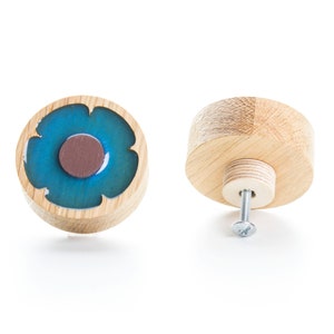 Può includere: Un pomello di legno con un design a fiore blu e marrone. Il pomello è mostrato da due angolazioni, una con la vite visibile e l'altra con il design del fiore rivolto verso la fotocamera.