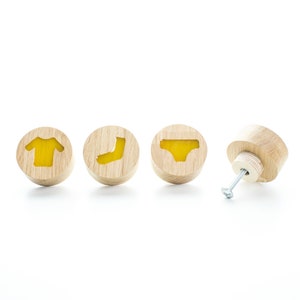 May include: Four wooden knobs with yellow accents. The knobs feature different clothing items: a t-shirt, a sock, underwear, and a blank knob.