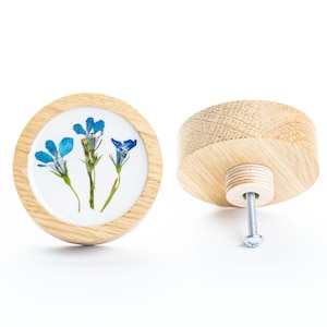 Può includere: Un pomello rotondo in legno con un design a fiori blu. Il pomello è mostrato da due angolazioni, una che mostra il davanti con il design floreale e l'altra che mostra il retro con la vite.