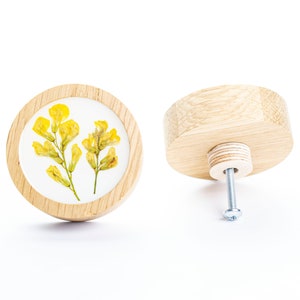 Puede incluir: Un pomo de madera redondo con un frente plano que presenta un diseño de flores amarillas prensadas. La parte posterior del pomo tiene un tornillo de metal.
