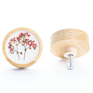 Peut inclure: Un bouton rond en bois avec un fond blanc et un motif de fleurs rouges pressées. Le bouton est doté d'une vis argentée pour la fixation à un tiroir ou une armoire.