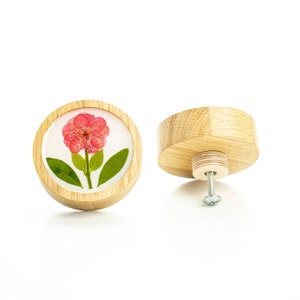 Può includere: Un pomello rotondo in legno con un fiore rosa pressato al centro. Il pomello è fissato a una vite per l'installazione.