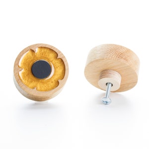 May include: Two wooden cabinet knobs with a gold flower design. One knob is shown from the front and the other from the back, revealing the screw.