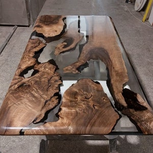 Könnte beinhalten: Eine große Tischplatte aus Holz mit einer klaren Epoxidharz-Oberfläche. Das Harz hat ein einzigartiges Muster aus schwarzen und weißen Wirbeln. Die Tischplatte wird von zwei schwarzen Metallbeinen getragen.