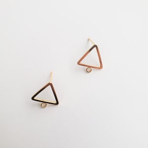 Peut inclure: Une paire de supports de boucles d'oreilles en forme de triangle dorés avec une petite boucle en bas. Les supports sont sur un fond blanc.
