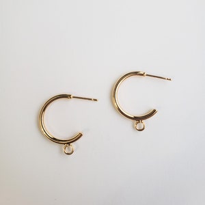 May include: A pair of gold hoop earrings with a small jump ring hanging from each hoop.