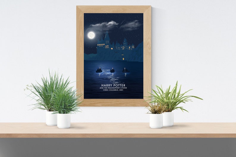 Puede incluir: Un p&oacute;ster enmarcado que representa una escena nocturna de la pel&iacute;cula "Harry Potter y la piedra filosofal". La obra de arte muestra un castillo en un lago bajo la luna llena, con el t&iacute;tulo de la pel&iacute;cula y el nombre del director en la parte inferior.