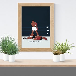 May include: A framed poster with a minimalist illustration of Muhammad Ali in a boxing match. The poster has a blue background with white text that reads "Muhammad Ali 1964".