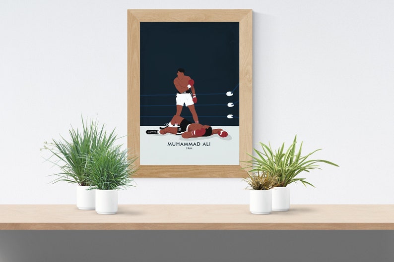 May include: A framed poster with a minimalist illustration of Muhammad Ali in a boxing match. The poster has a blue background with white text that reads "Muhammad Ali 1964".
