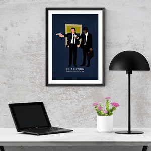 May include: A framed art print featuring a minimalist illustration of two figures from the movie Pulp Fiction. The artwork is set against a dark blue background, with the film's title and director's name at the bottom. The print is displayed on a white desk.