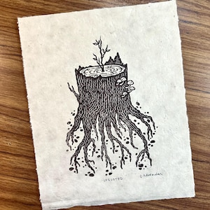 May include: A black and white linocut print on textured paper depicts a tree stump with exposed roots and a small plant growing from the top. The word "UPROOTED" is printed at the bottom, along with the artist's signature.