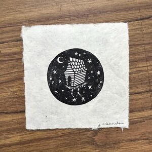 May include: Black and white illustration of a whimsical house with legs, set within a starry night sky and crescent moon. The artwork is on a textured, square piece of paper, signed "j. alexander".