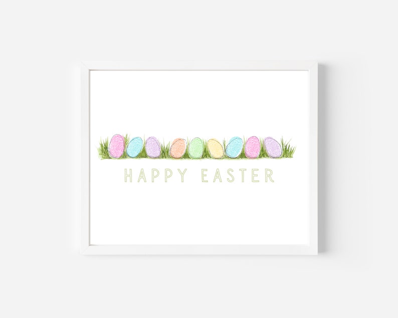 May include: A white framed print featuring a row of pastel coloured Easter eggs on a green grass background. The text "HAPPY EASTER" is written in a light green font below the eggs.