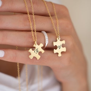 May include: Two gold necklaces with puzzle piece pendants. The pendants are engraved with the letters "K" and "V".