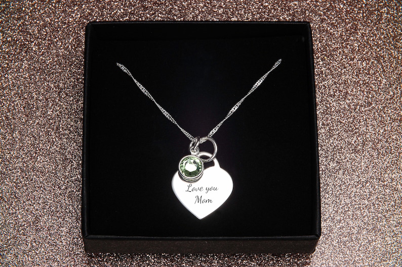 May include: Silver necklace with a heart pendant that says "Love you Mom" and a small green gemstone. The necklace is in a black box.