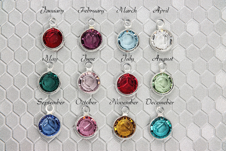 May include: Twelve silver charms with colored crystals, each representing a different month of the year. The charms are arranged in four rows of three, with the month name printed above each charm.