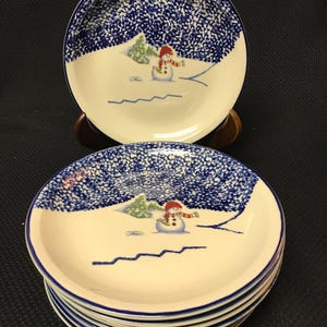 May include: Set of six blue and white ceramic bowls with a snowman design. The bowls have a speckled blue glaze and a blue rim.