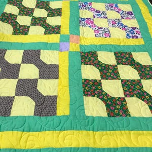 May include: A handmade quilt with a patchwork design. The quilt features squares of yellow, green, and floral patterned fabric. The quilt has a green border with yellow accents and a quilted pattern.