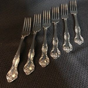 May include: Set of seven silver forks with ornate handles. The forks have a traditional design with a decorative floral pattern.