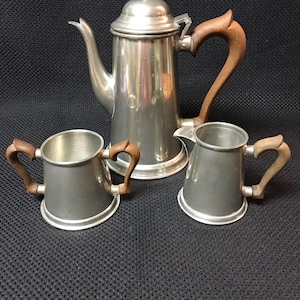 May include: A pewter tea set with wooden handles. The set includes a teapot, creamer, and sugar bowl.
