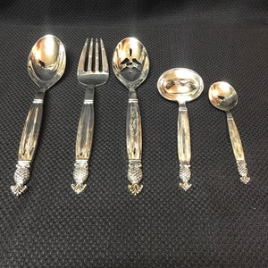 May include: A set of five silver-plated serving utensils with pineapple-shaped handles. The set includes a large spoon, a slotted spoon, a fork, a ladle, and a small spoon.