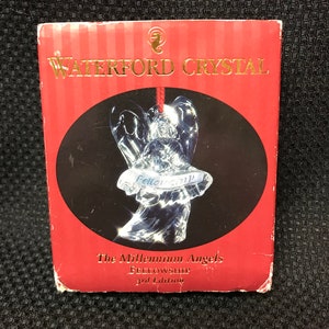 May include: A clear crystal angel ornament with the words "Fellowship" inscribed on the base. The ornament is packaged in a red box with gold lettering that reads "Waterford Crystal" and "The Millennium Angels Fellowship 3rd Edition".