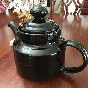 May include: A black ceramic teapot with a shiny finish and a rounded body. The teapot has a lid with a knob on top.