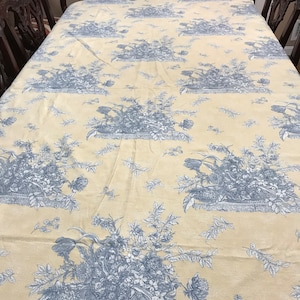 May include: A yellow tablecloth with a blue floral pattern. The pattern features baskets of flowers and leaves.