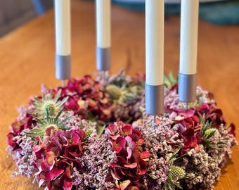 May include: A festive Advent wreath with four white candles, each set in a silver holder, arranged in a circle. The wreath is composed of burgundy hydrangeas, purple heather, and green thistle, creating a seasonal centerpiece.