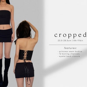 Puede incluir: Top de cors&eacute; negro sin tirantes con la espalda con cordones y ojales plateados. El top mide de 23,5 a 28,5 cm de largo y tiene 12 canales de ballenas. El texto "cropped" y "features:" es visible en la imagen. El texto debajo de "features:" dice "princess seam bodice", "12 boning channels", y "eyelet back closure".