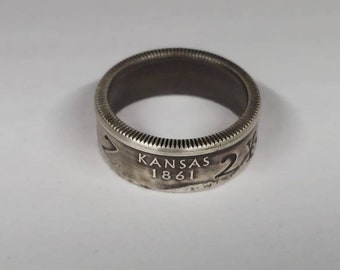 May include: A silver ring made from a Kansas state quarter. The ring features the inscription "Kansas 1861" on the band.