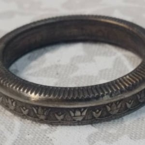May include: A silver ring with a decorative design of stylized flowers around the band.