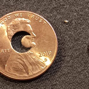 May include: A copper penny with a hole cut out in the shape of a crescent moon. The penny is dated 2019 and has the words "In God We Trust" and "Liberty" inscribed on it. The crescent moon piece is also shown separately.