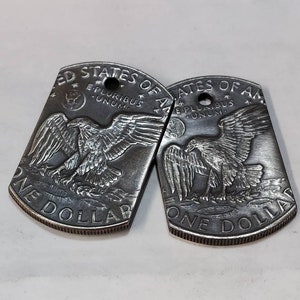 May include: Two silver-toned metal dog tags with a design of an eagle and the words "United States of America" and "One Dollar" on each tag.